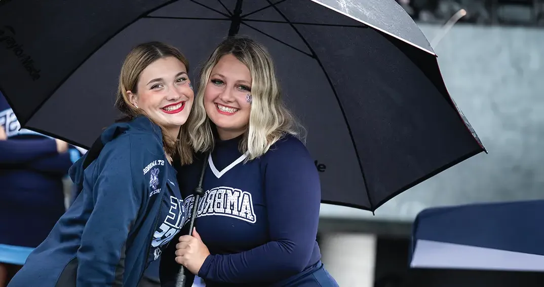 Two cheerleaders standing under and umbrella.